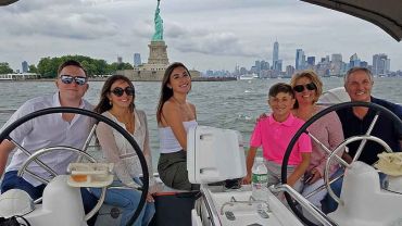 At the helm of a sailboat posing for photos with the Statue Of Liberty