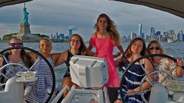 Girls at the helm of a sailboat at the Statue Of Liberty