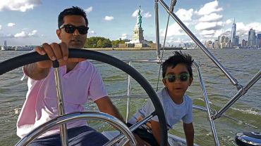 Father and son sailing at the helm near the Statue Of Liberty