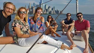 Group of six people on the bow of a sailboat with Manhattan skyline